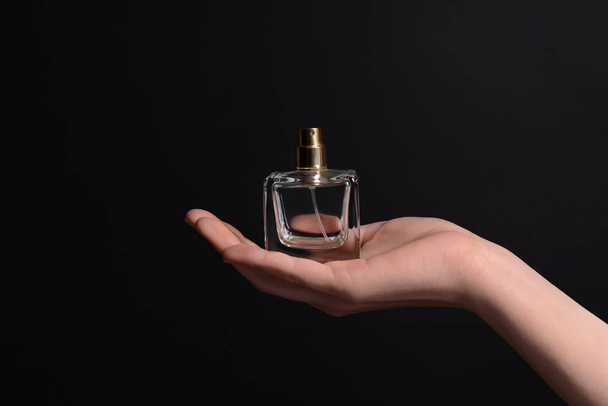 Mujer sosteniendo botella de perfume sobre fondo oscuro
 - Foto, Imagen