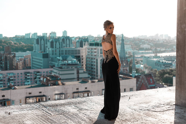 блондинка в черном вечернем платье. гламурная молодая женщина. вид на город
 - Фото, изображение