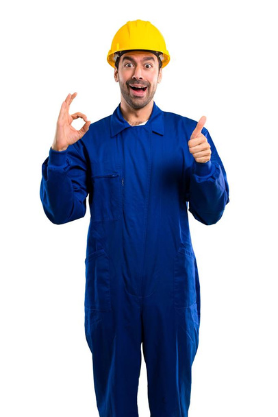 Young workman with helmet showing an ok sign with fingers and giving a thumb up gesture with the other hand on isolated white background - 写真・画像