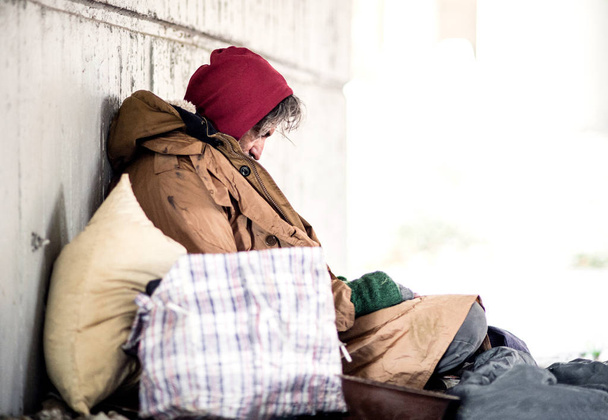 A side view of homeless beggar man sitting outdoors, leaning against a wall. Copy space. - Fotografie, Obrázek