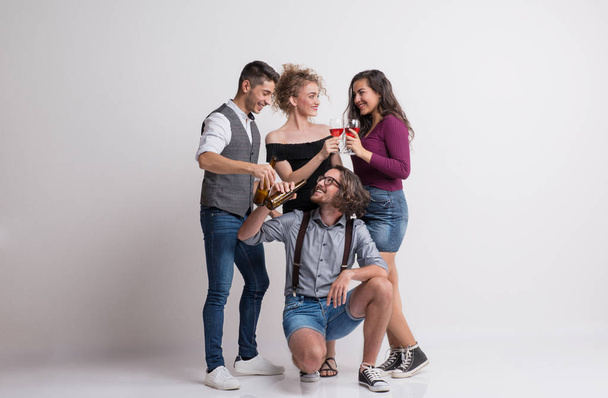 Portrait of young group of friends standing in a studio, holding bottles and glasses. - Foto, afbeelding