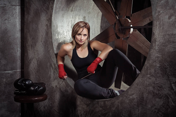 スポーツのボクシング包帯と暗いスタジオ カメラ目線で周りのボクシング グローブで金髪の女性。強い女性の概念. - 写真・画像