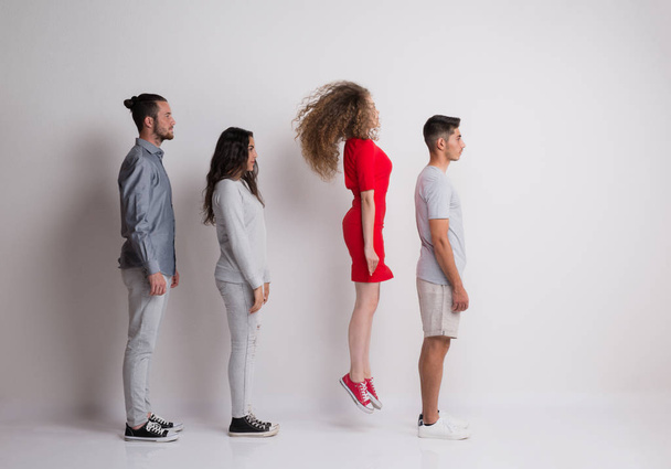 Side view of young group of friends standing in a studio, one is jumping. - Foto, afbeelding