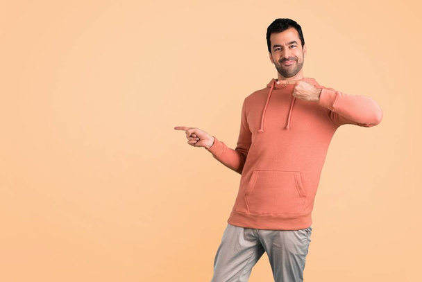 Man in a pink sweatshirt pointing finger to the side and presenting a product while smiling on ocher background - Fotografie, Obrázek