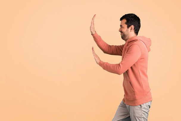 Man in a pink sweatshirt pushing something on ocher background - Foto, Imagem