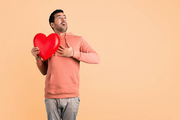 Man in a pink sweatshirt holding a big heart icon toy on ocher background - Valokuva, kuva