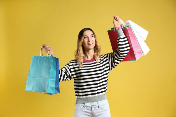 Красивая молодая женщина с пакетами покупок на цветном фоне - Фото, изображение