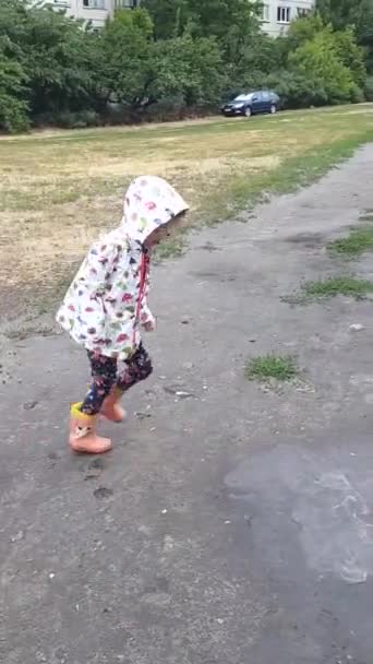 Μικρό κορίτσι άλματα στην μπότες από καουτσούκ σε μια λακκούβα. - Πλάνα, βίντεο