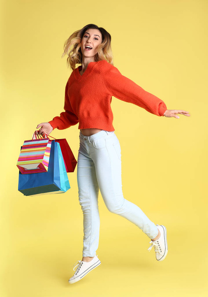 Zorgeloos jonge vrouw met boodschappentassen op kleur achtergrond - Foto, afbeelding