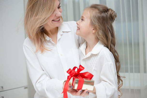 Daughter giving her mother a christmas present at home in the living room - 写真・画像