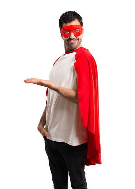 Homem super-herói com máscara e capa vermelha apresentando um produto ou uma ideia enquanto olha sorrindo em direção a fundo branco isolado
 - Foto, Imagem