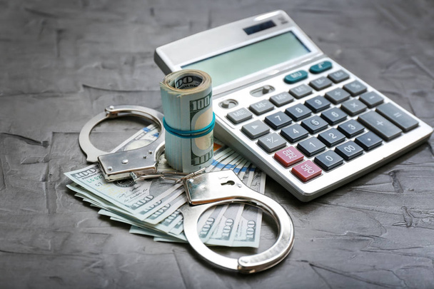 Dollar banknotes with handcuffs and calculator on grey table. Corruption concept - Photo, Image