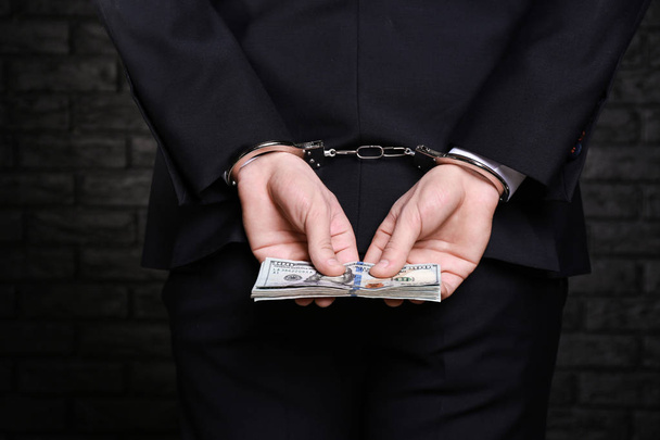 Businessman in handcuffs with bribe on dark background - Foto, Imagen