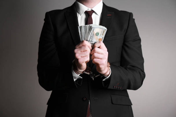 Geschäftsmann in Handschellen mit Schmiergeld vor grauem Hintergrund. Korruptionskonzept - Foto, Bild