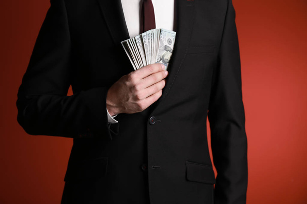 Businessman hiding dollar banknotes in jacket on color background. Corruption concept - Foto, imagen