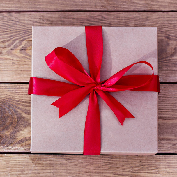 Kraft-Box für Geschenke mit einer Schleife auf Holzbrettern gebunden. Schnur oder Faden in einer Schleife auf Kraftpapier Geschenkschachtel ohne Holztisch Textur und Hintergrund gebunden. - Foto, Bild