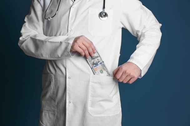 Doctor putting bribe in pocket on color background. Corruption concept - Photo, Image