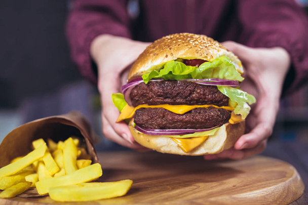 Mains tenant de délicieux hamburgers frais avec des frites sur la table en bois
  - Photo, image