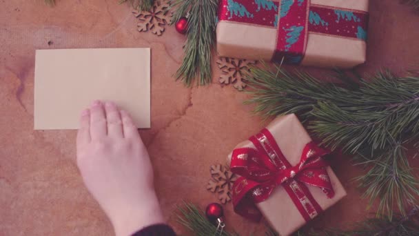 Gelukkig Kerstmis concept met boom pijnboomtakken, geschenkdozen en hand leeg kaart op tafel zetten - Video