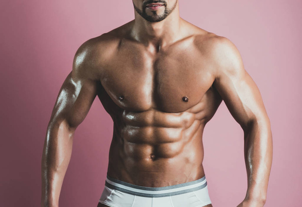Sport. Portrait of strong healthy handsome athletic man's body. Close up of fitness model posing near pink wall. Perfect muscular chest of young sportsman. Athletic body type and atriptease theme - Photo, Image