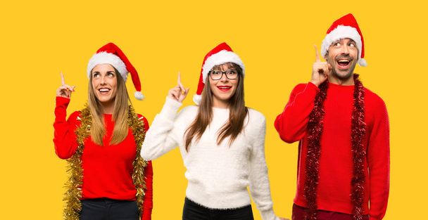 A group of people Blonde woman dressed up for christmas holidays intending to realizes the solution while lifting a finger up on yellow background - Photo, Image