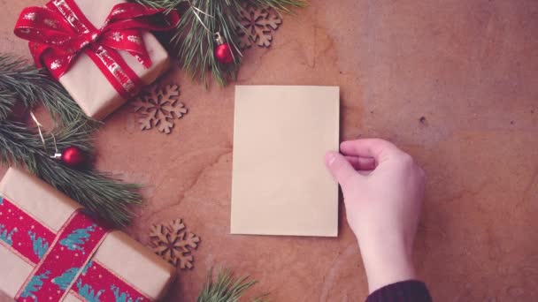 Boldog karácsonyi concept fenyő fa ágai, díszdobozok és kéz táblázat üres kártya felhelyezése - Felvétel, videó