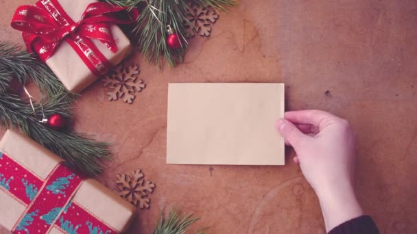 Boldog karácsonyi concept fenyő fa ágai, díszdobozok és kéz táblázat üres kártya felhelyezése - Felvétel, videó