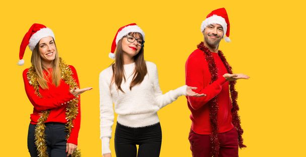 A group of people Blonde woman dressed up for christmas holidays presenting an idea while looking smiling towards on yellow background - Φωτογραφία, εικόνα
