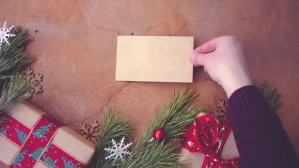 Feliz concepto de Navidad con ramas de pino, cajas de regalo y la mano poniendo tarjeta en blanco en la mesa
 - Metraje, vídeo