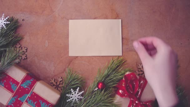 Hyvää joulua konsepti mänty oksat, lahjapakkaukset ja käsi laskemisesta tyhjä kortti pöydälle
 - Materiaali, video