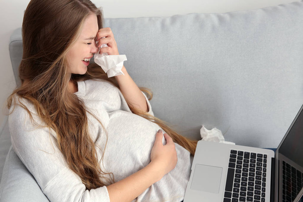 Mujer embarazada joven con portátil llorando en casa debido a un cambio de humor
 - Foto, Imagen