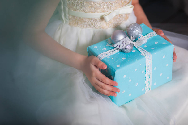 Little girl in white dress holds box with New Year's gift in hand - Fotografie, Obrázek