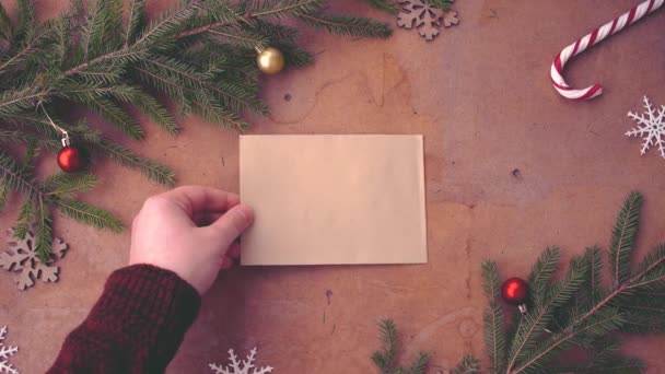 Gelukkig Kerstmis concept met boom pijnboomtakken, decoraties en hand leeg kaart op tafel zetten - Video