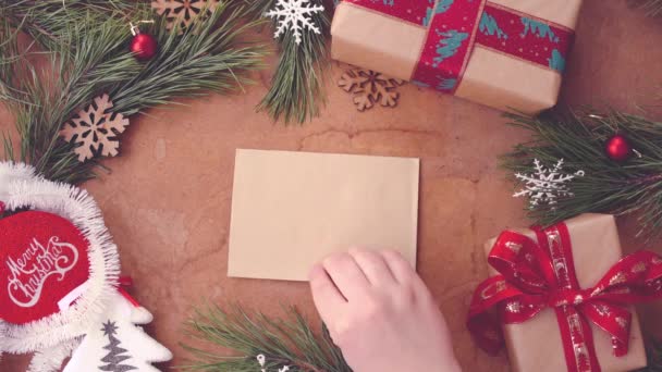 Feliz concepto de Navidad con ramas de pino, cajas de regalo y la mano poniendo tarjeta en blanco en la mesa
 - Metraje, vídeo