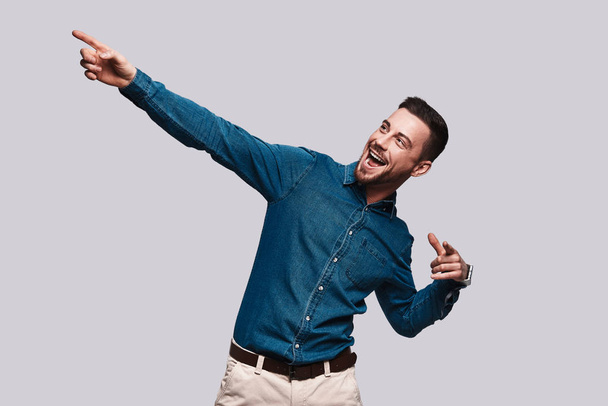 happy handsome young man pointing finger on left side, copy space grey background - Foto, imagen