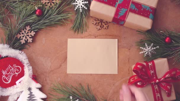 Šťastné Vánoce koncept borových větví, dárkové krabičky a rukou uvedení prázdné karty na stole - Záběry, video