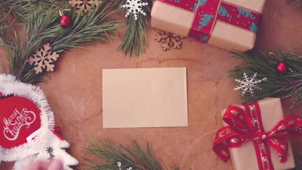 Щаслива різдвяна концепція з гілками сосен, подарунковими коробками та рукою, що кладе порожню картку на стіл
 - Кадри, відео
