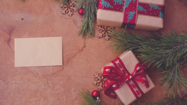 Hyvää joulua konsepti mänty oksat, lahjapakkaukset ja käsi laskemisesta tyhjä kortti pöydälle
 - Materiaali, video