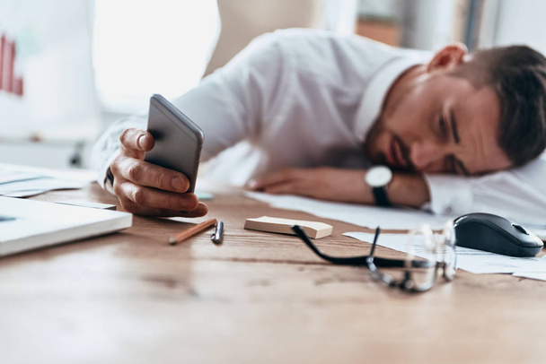 tired businessman lying on desk and browsing mobile phone  - Фото, зображення