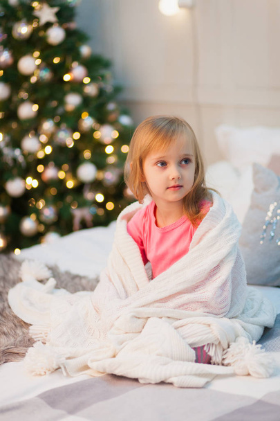 Cute little girl in pink pajamas on the background of the Christmas tree - Foto, Imagen