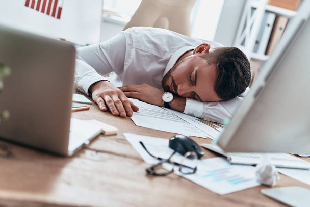 Tired businessman lying on table in office and sleeping  - Fotó, kép