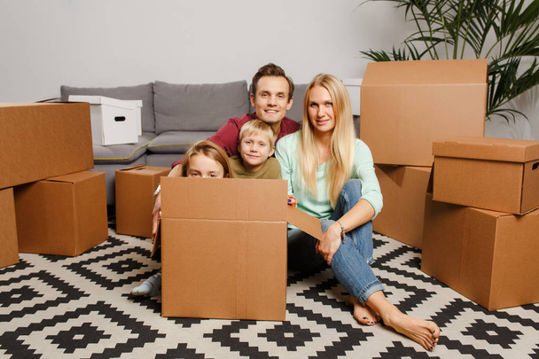 Photo of young couple with son and daughter sitting on floor among cardboard boxes - Foto, Imagen