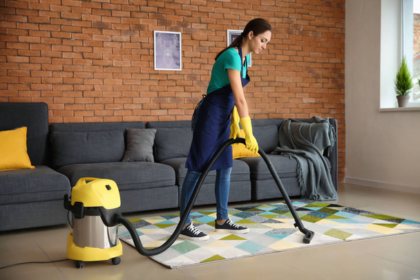 Женщина-уборщица пылесосит ковер в квартире
 - Фото, изображение