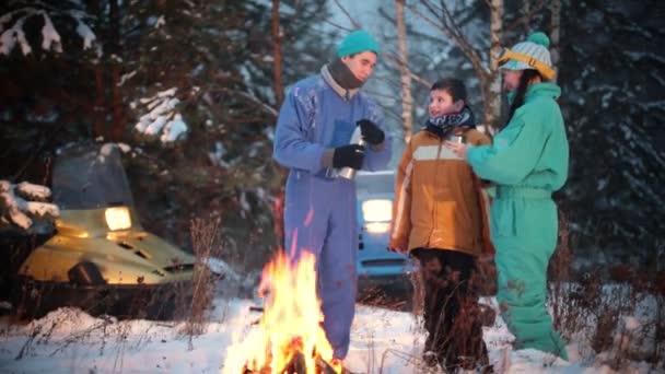 Winterwald. junge Familie steht im Wald am Feuer und trinkt heiße Getränke aus der Thermoskanne. - Filmmaterial, Video