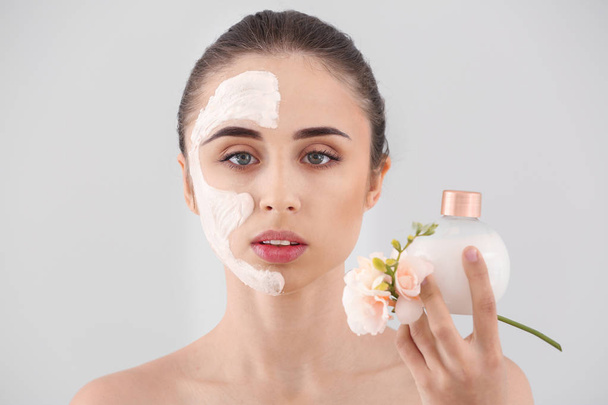 Beautiful young woman with facial mask and cream on light background - Photo, Image