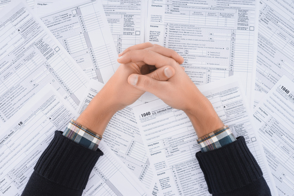 weergave van man met gevouwen handen op achtergrond met belastingformulieren bijgesneden - Foto, afbeelding