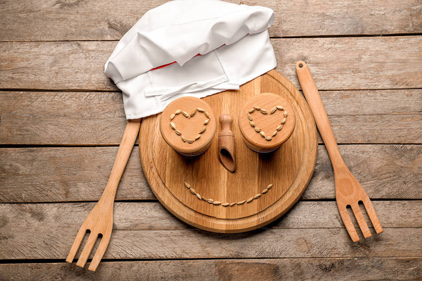 Creative composition with chef's hat, cutting board and kitchen utensils on wooden background - Фото, изображение
