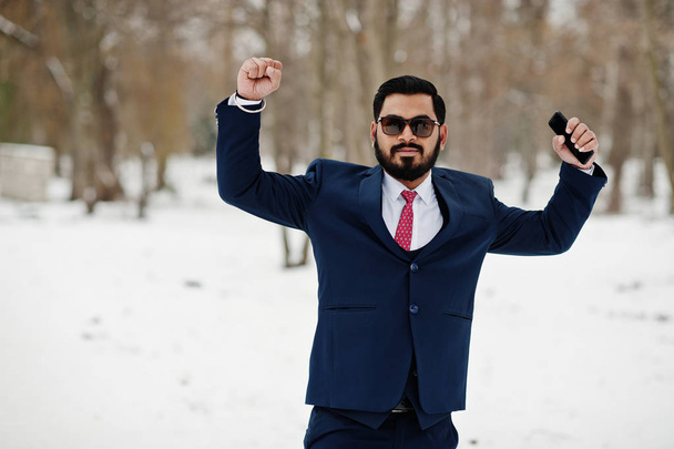 Stylish indian beard business man in suit and sunglasses posed at winter day outdoor, hands up and happy emotions. - 写真・画像