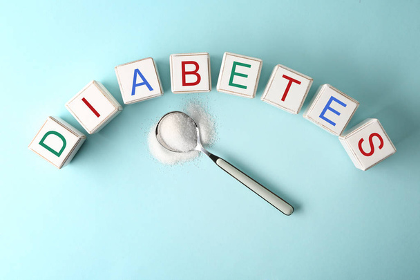 Kubussen vormen woord Diabetes en lepel met suiker op kleur achtergrond - Foto, afbeelding