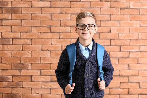 Cute little schoolboy with backpack against brick wall - Фото, зображення